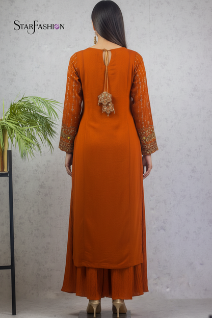 A woman is shown from the back wearing a rust-orange traditional Indian outfit with embroidered sleeves and a decorative tie at the back, standing against a textured gray wall. The brand name 'STARFASHION' is visible in the top left corner.