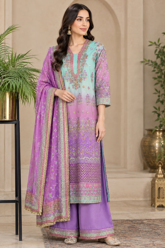 A woman models a traditional three-piece Indian salwar kameez suit. The set features a lavender and mint green gradient kurta with intricate gold embroidery, matching wide-leg trousers, and a coordinating sheer dupatta with a gold border.