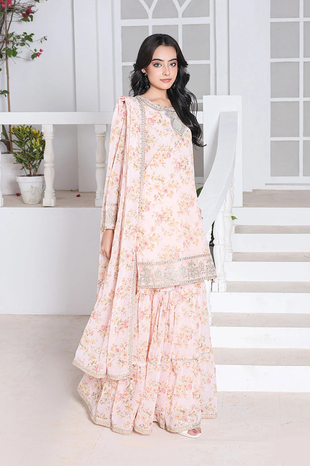 Woman in a floral dress standing in a bright room with white walls and a staircase.