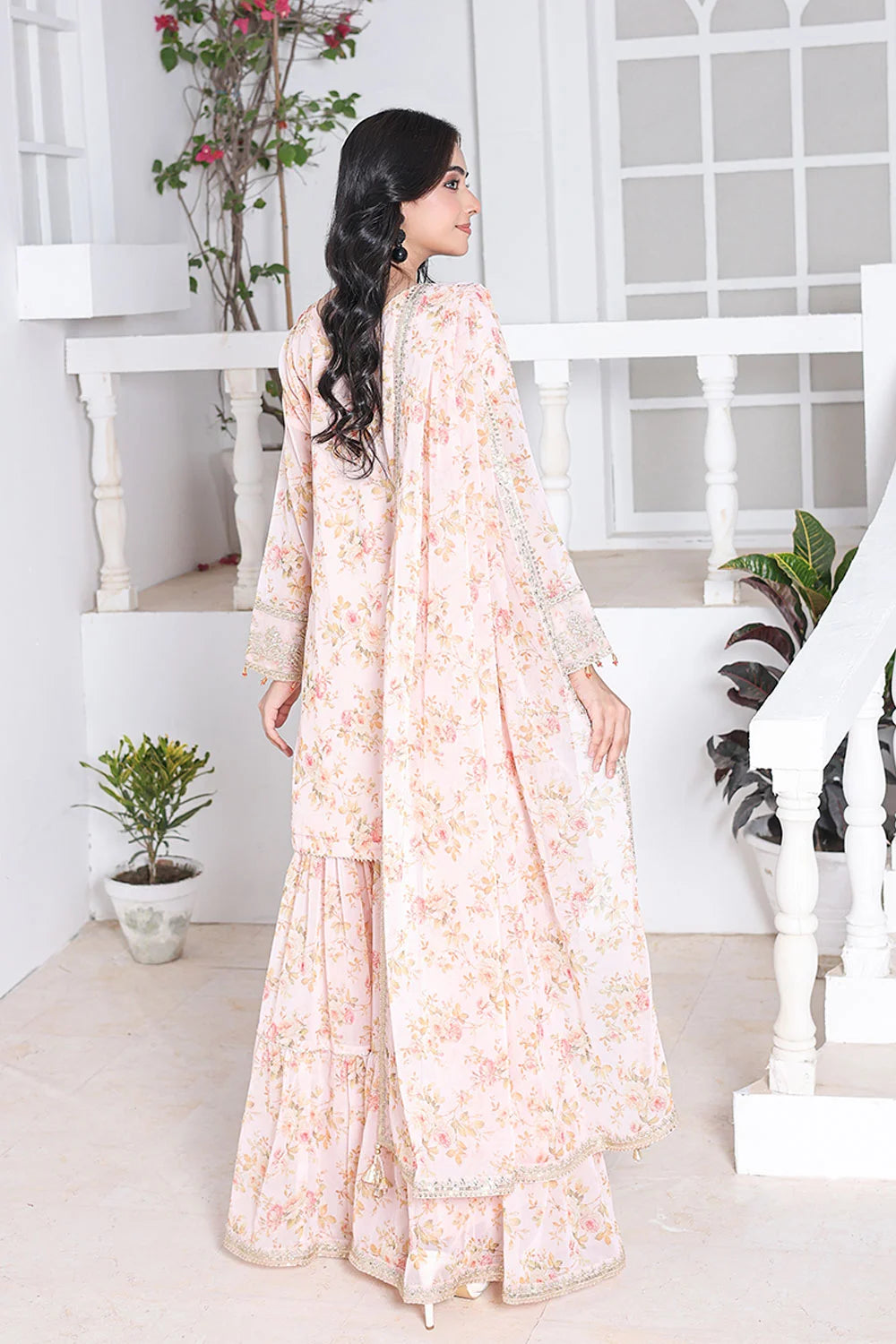 Woman in a floral dress standing in a bright, minimalistic room with white walls and a staircase.