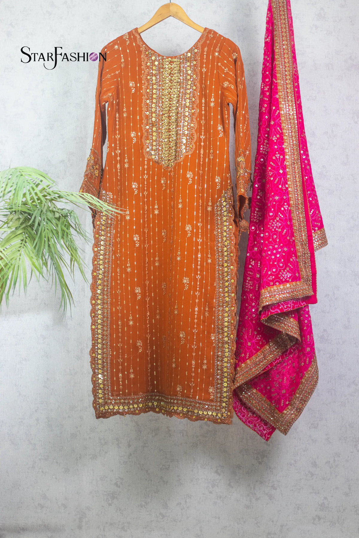 Orange embroidered kurta with pink dupatta on a hanger against a gray wall.