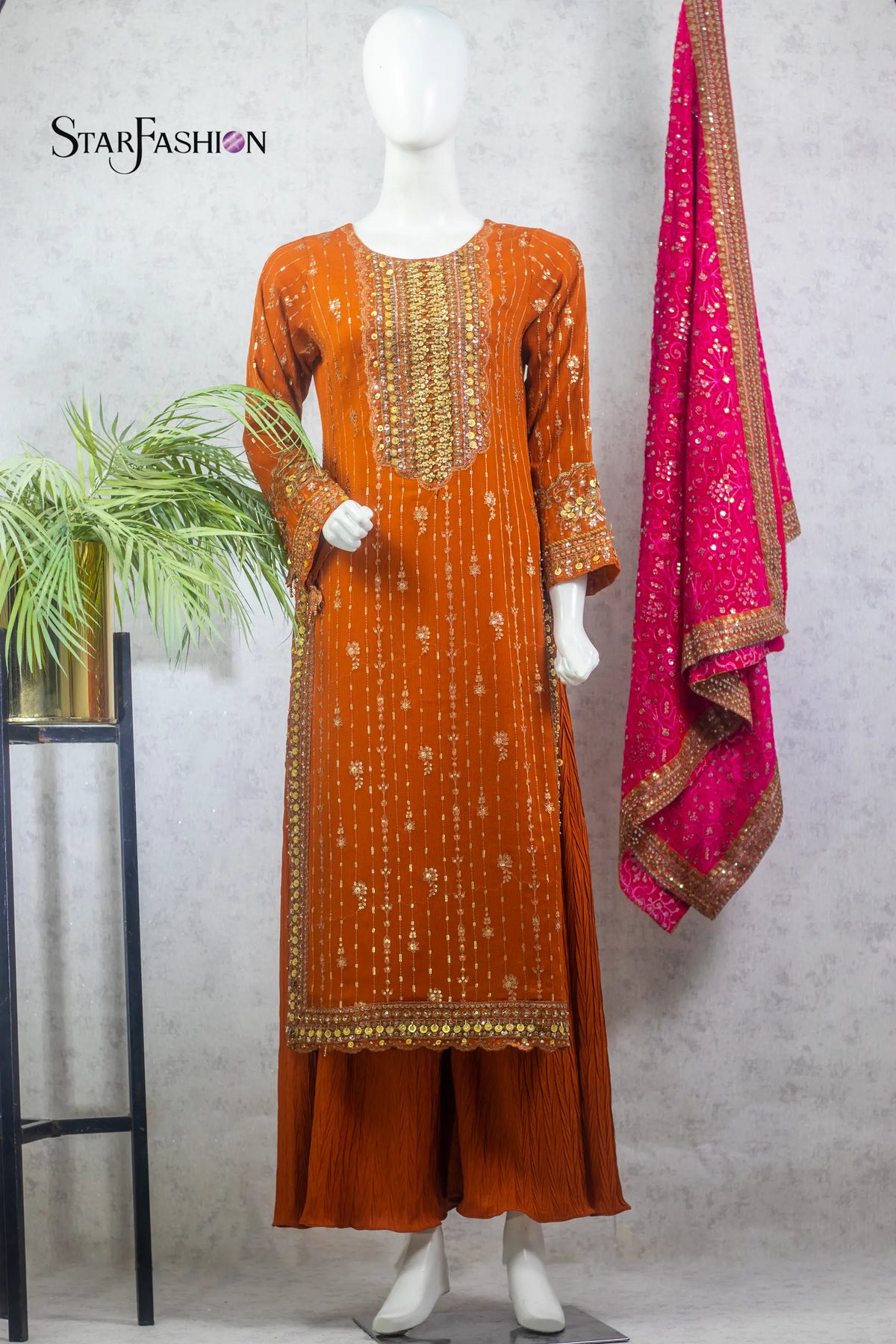 Orange embroidered outfit with pink dupatta on a mannequin against a gray background